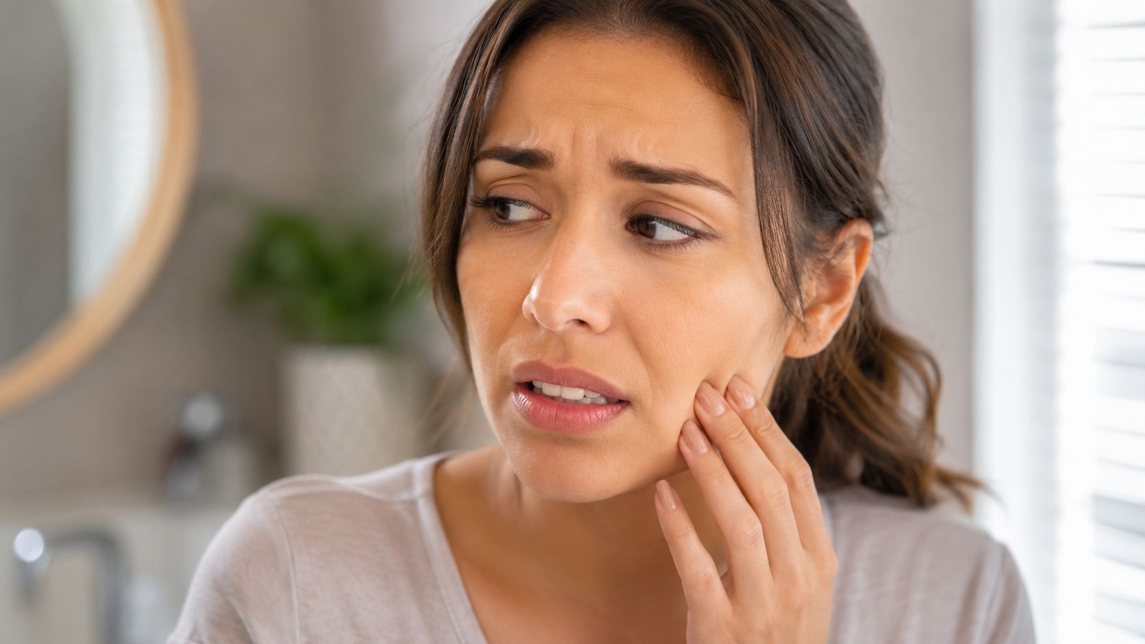 A woman experiencing tooth pain while touching her cheek, reflecting potential discomfort related to dental procedures.