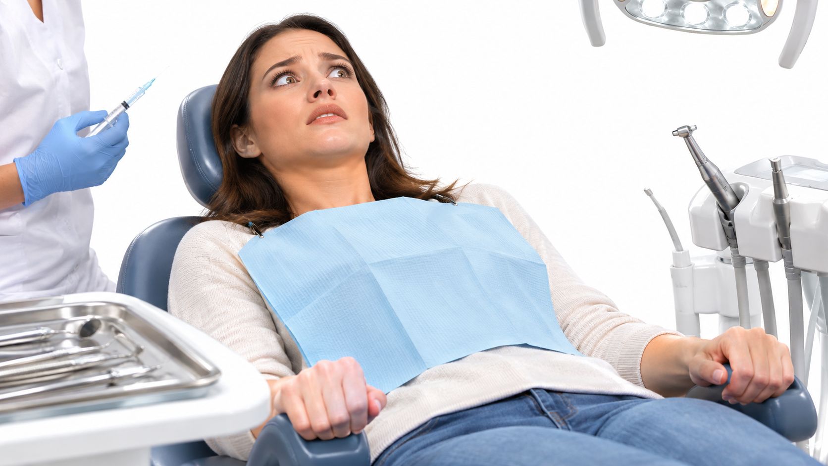 A nervous patient sitting in a dental chair looking anxiously at a syringe held by the dentist.